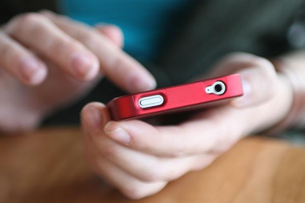 person holding a red mobile phone in their hand while tapping on the screen with the other hand