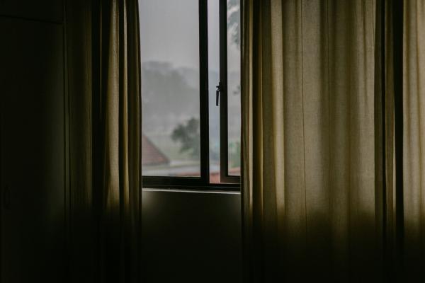 a window ajar with cream curtains hanging beside it